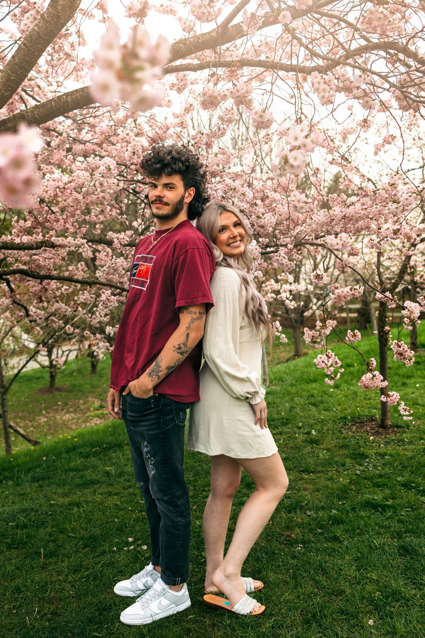 Romantic couple posing under blooming cherry blossom trees in spring.