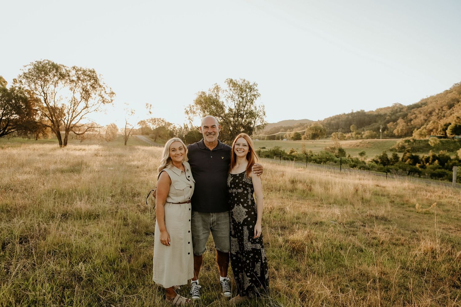 A group of people stand together in a golden field at sunset with mountains in the background.