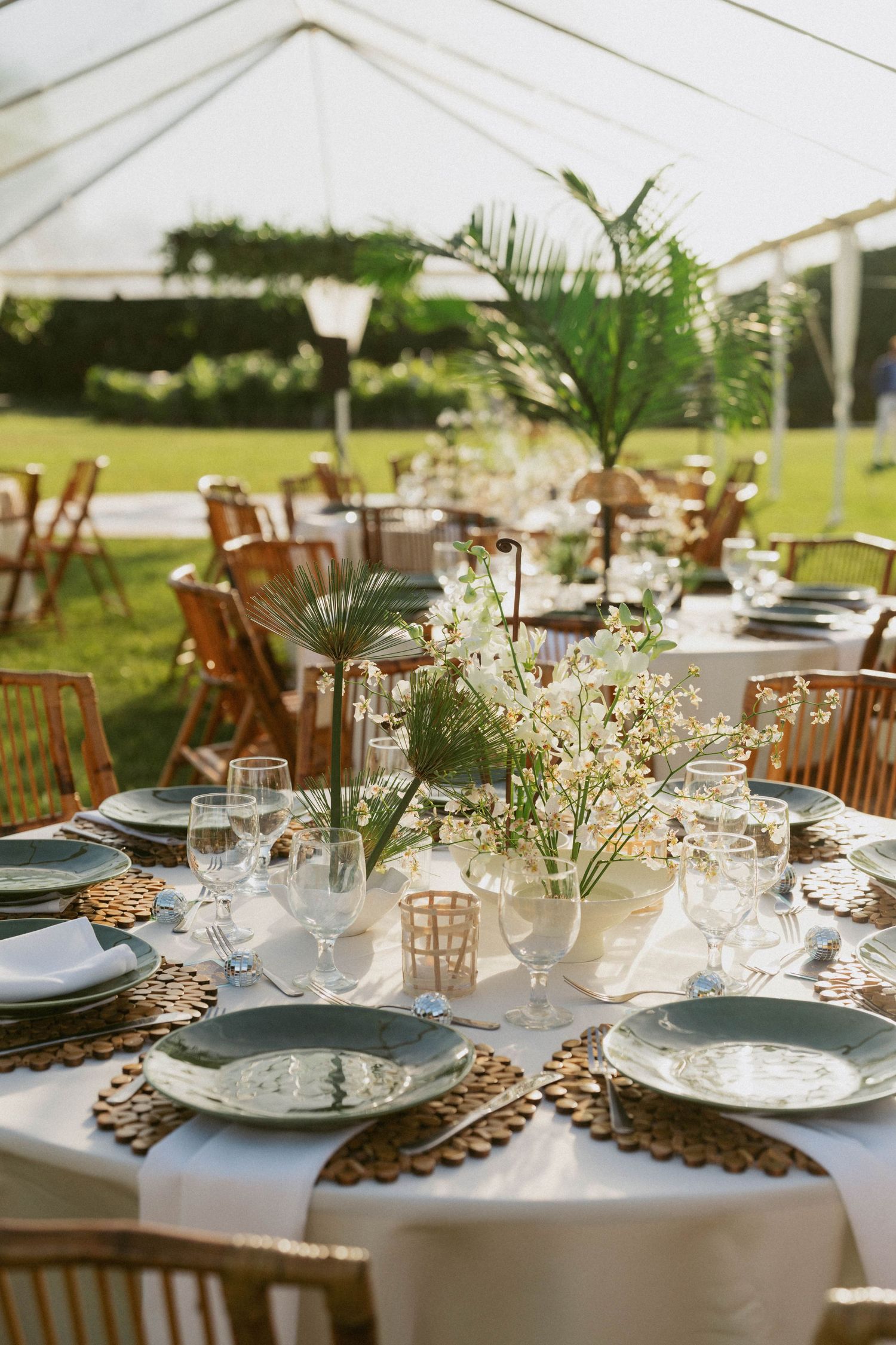 Elegant outdoor wedding reception tables set with white linens, wooden chairs, and delicate floral centerpieces.