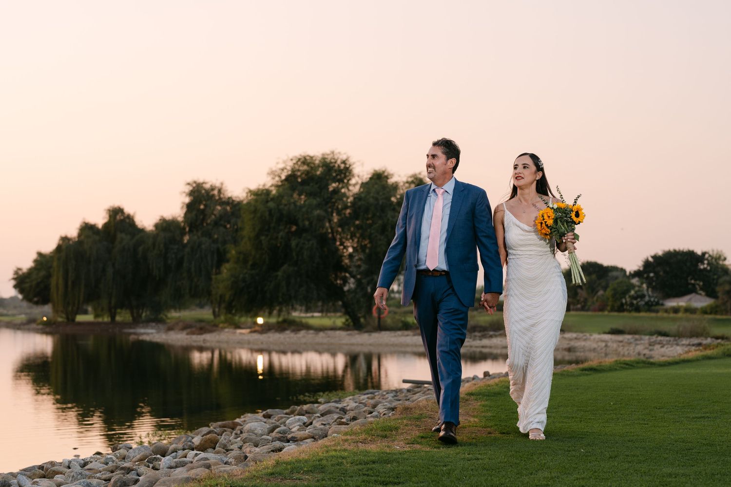 A newlywed couple poses against Dubai's modern skyline with white floral decorations.