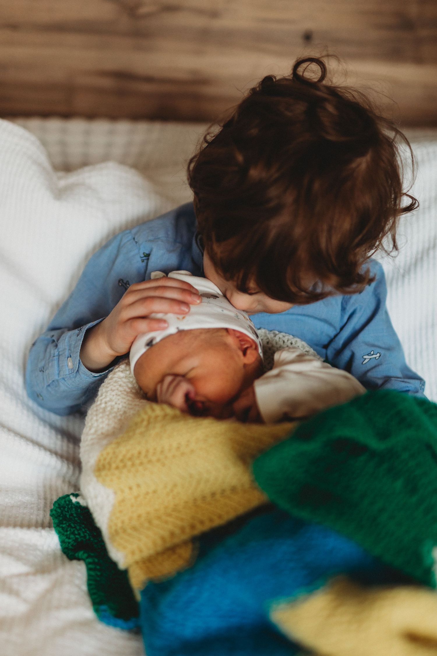 A tender moment between siblings as they lie together on colorful knit blankets in soft lighting.