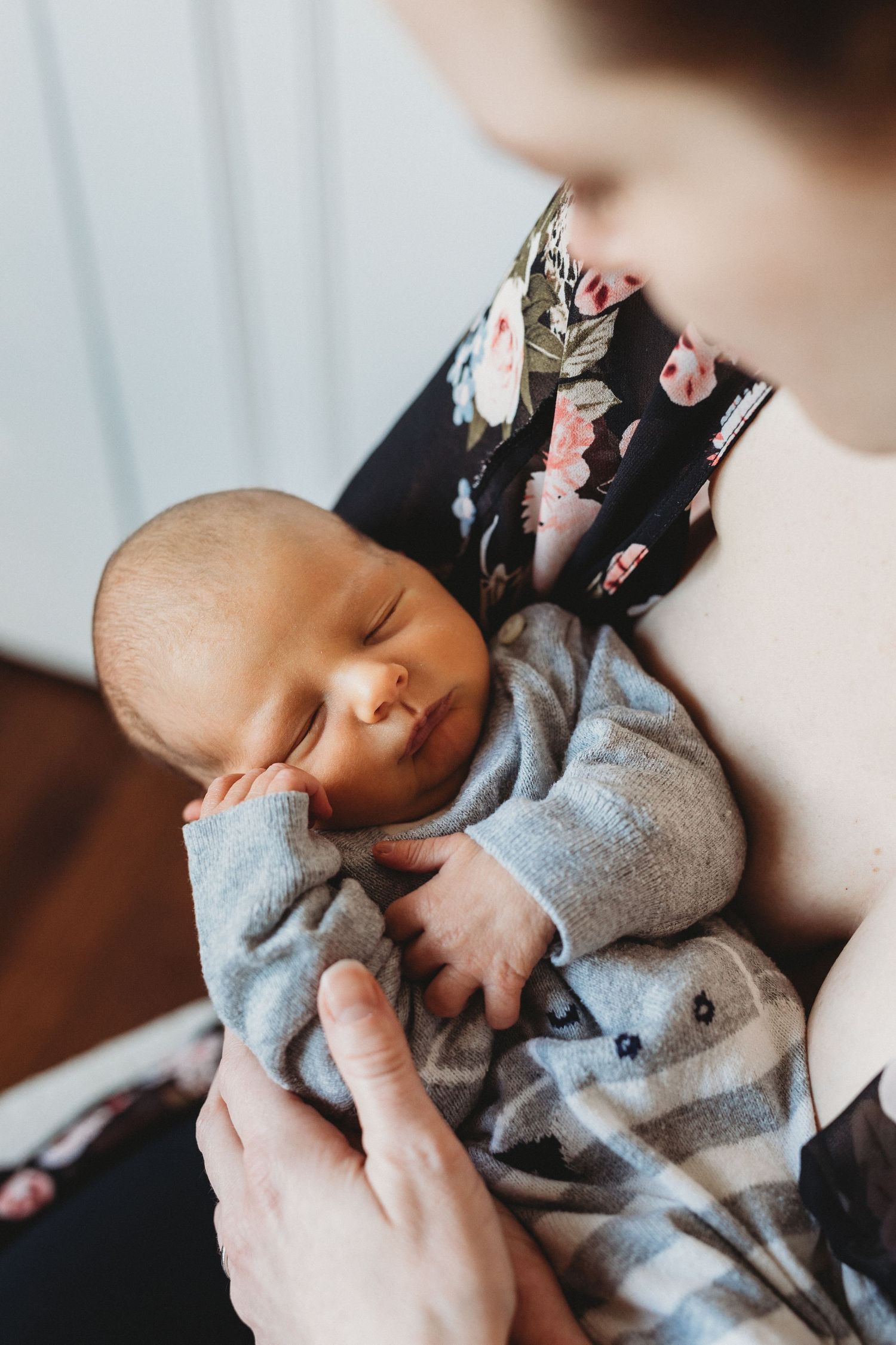 Peaceful sleeping newborn in a gray sleeper outfit being cradled gently while holding a small stuffed toy.