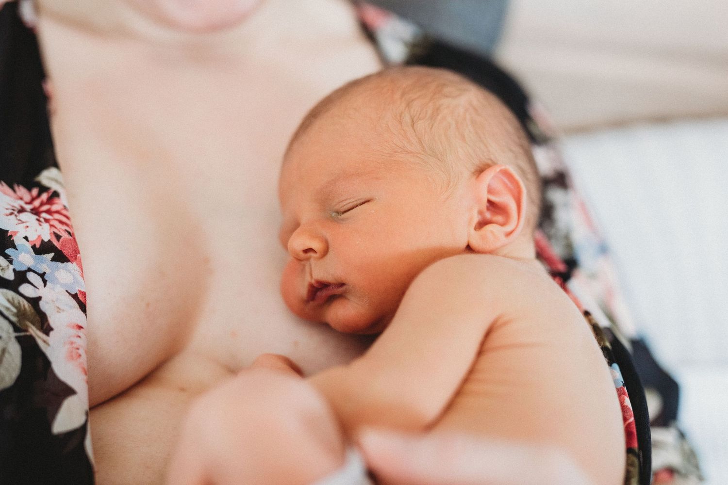 A peaceful sleeping newborn baby rests against someone wearing a floral print top.