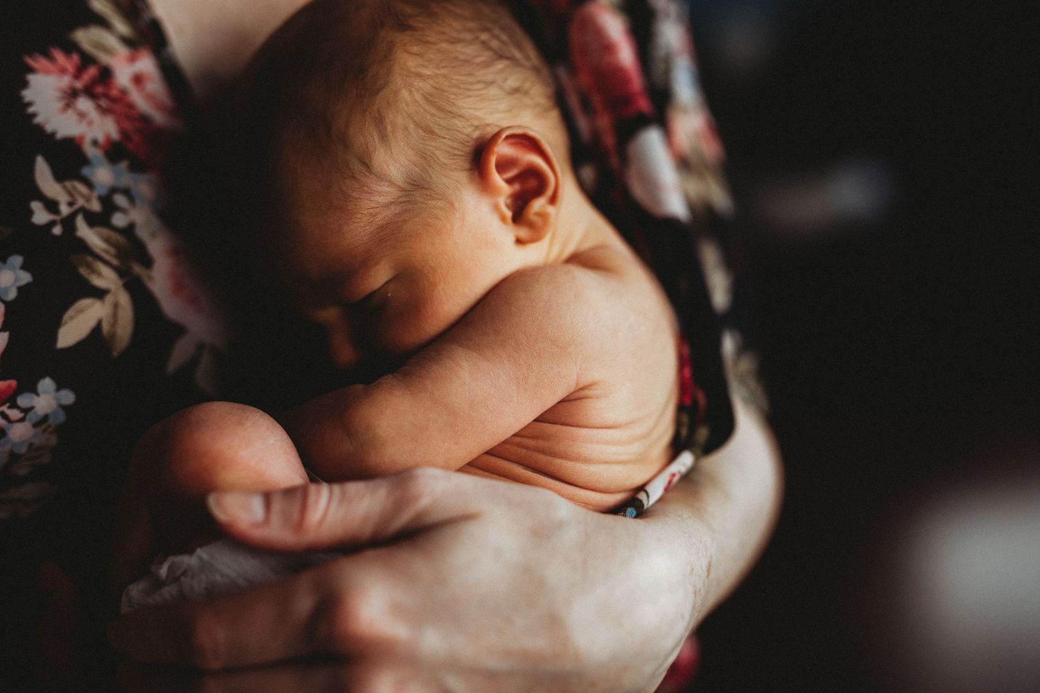 A sleeping newborn baby wrapped in a floral blanket lies peacefully in gentle lighting.
