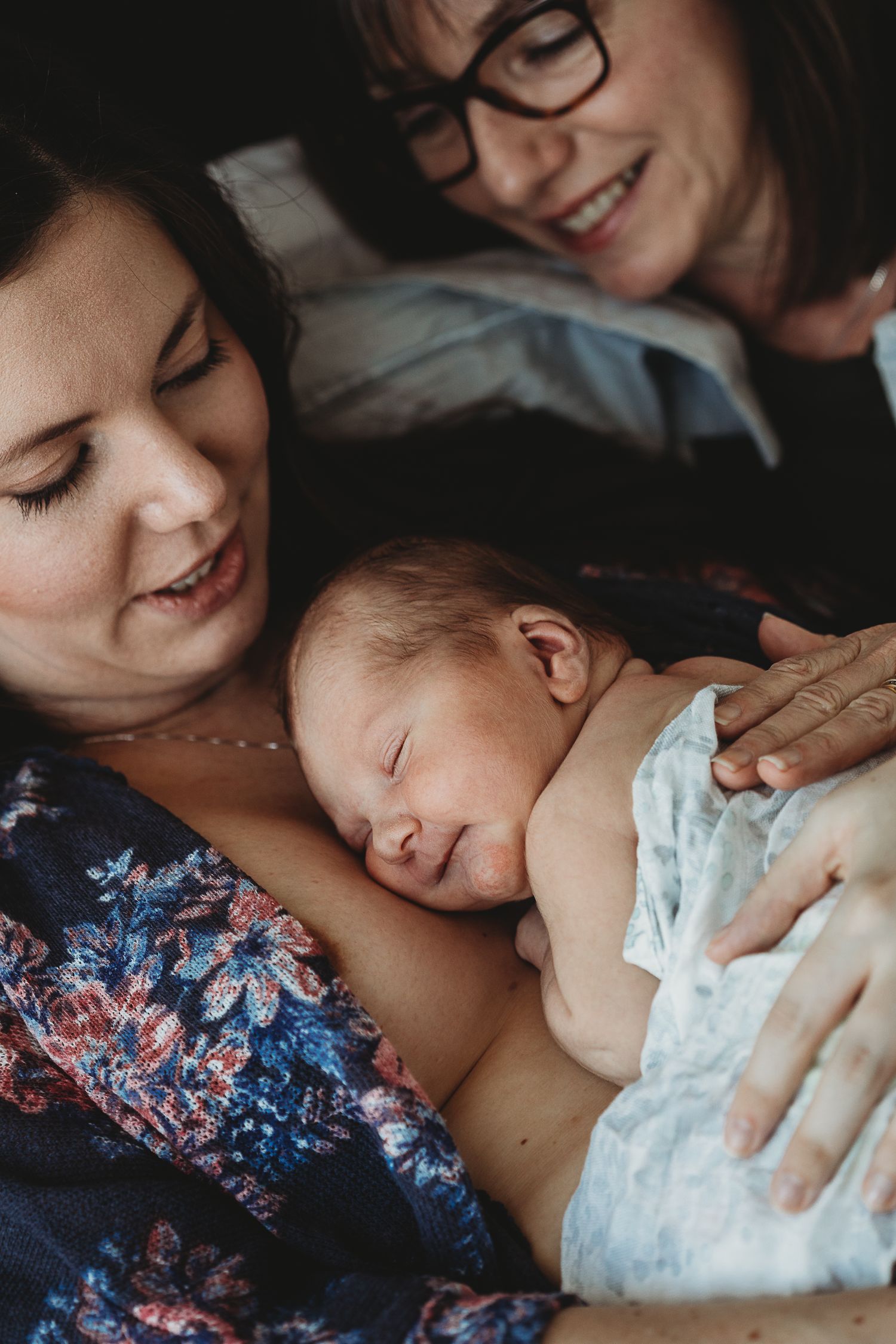 A tender moment of a sleeping newborn nestled against someone in a floral dress while being comforted.