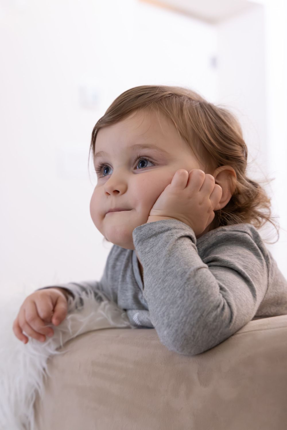 A small child in a gray sweater rests their head on their hand while daydreaming.