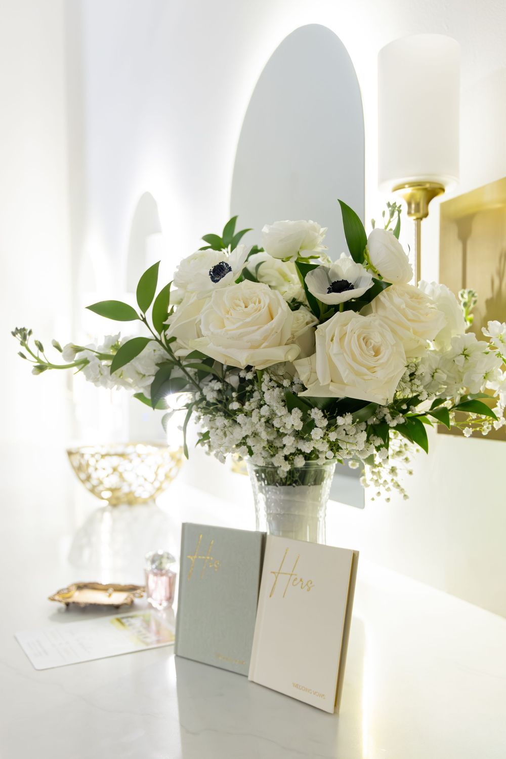 Elegant white roses and greenery arranged in white vases with place cards for a wedding reception.