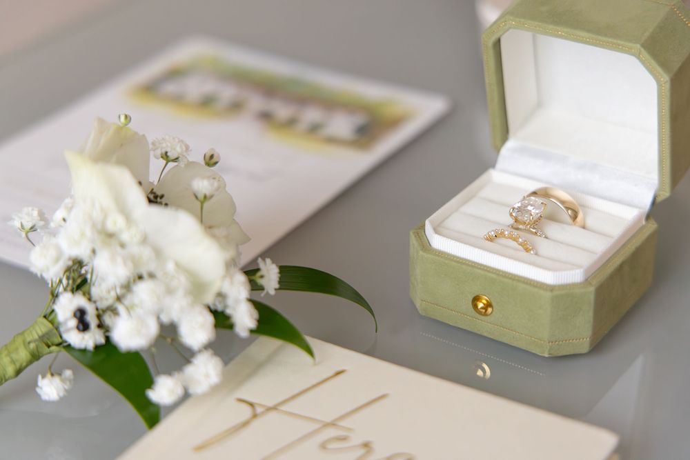White floral ring boxes with gold accents display delicate wedding rings against a soft gray backdrop.