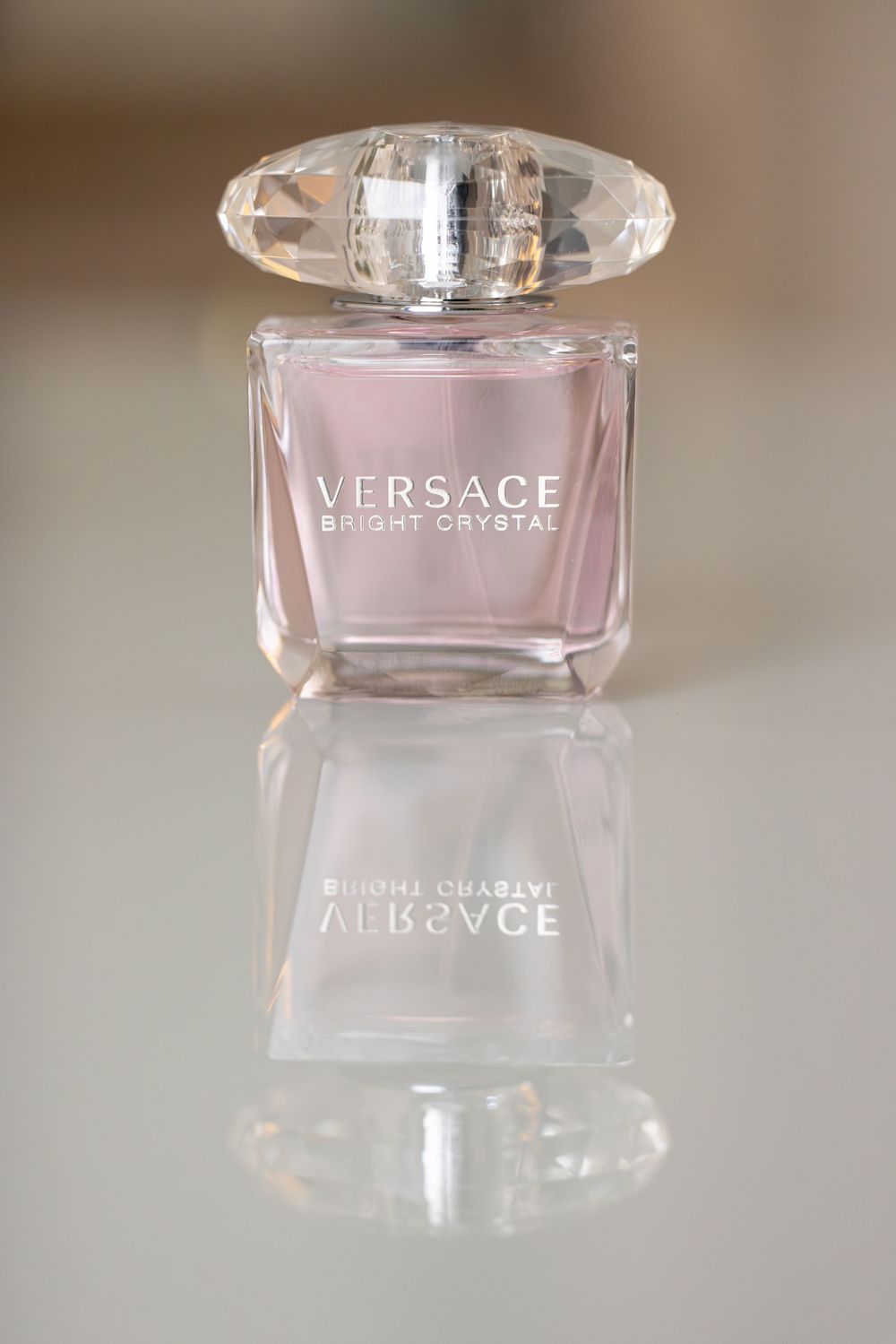 Pink perfume bottles of Versace Bright Crystal fragrance displayed on reflective surface.