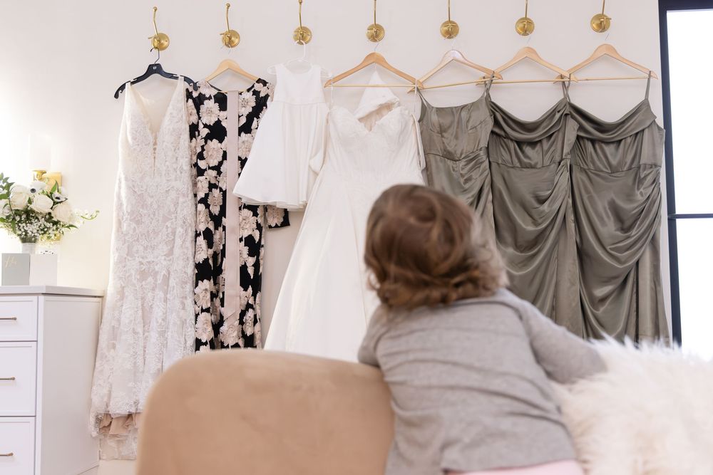 Wedding dresses hang on display in a bridal boutique with floral wallpaper and elegant lighting fixtures.