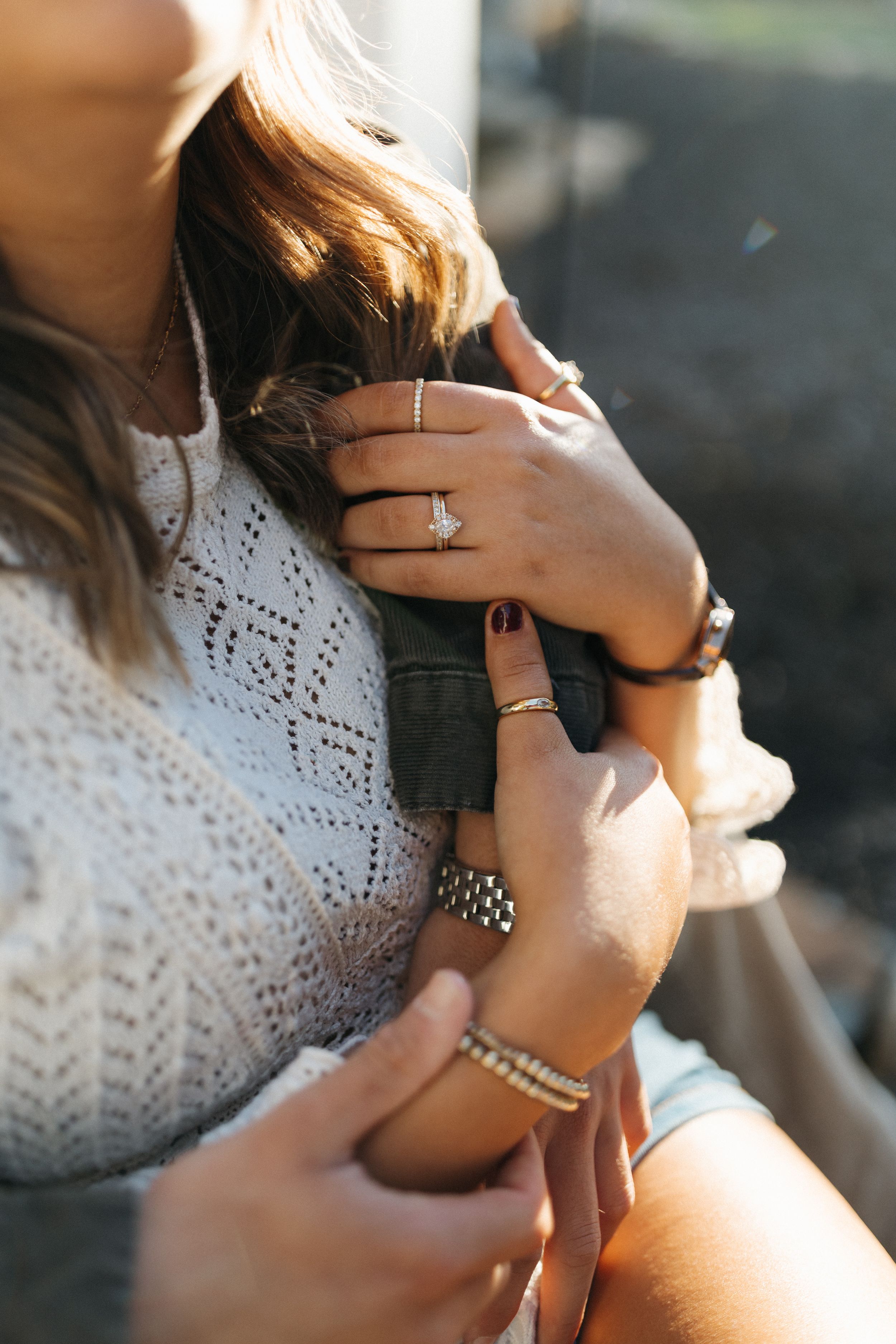 Close-up shots of hands wearing delicate silver rings and bracelets against white lace clothing in natural sunlight.