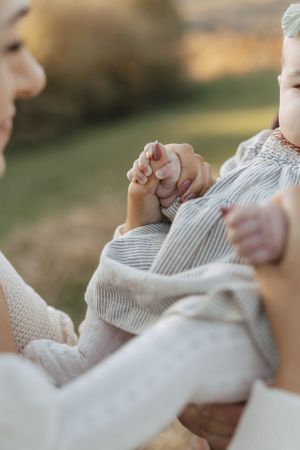 Close-up shot of tiny hands grasped together in a tender family moment outdoors.