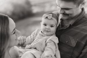 Black and white intimate family portrait showing tender moment with baby in knit sweater.