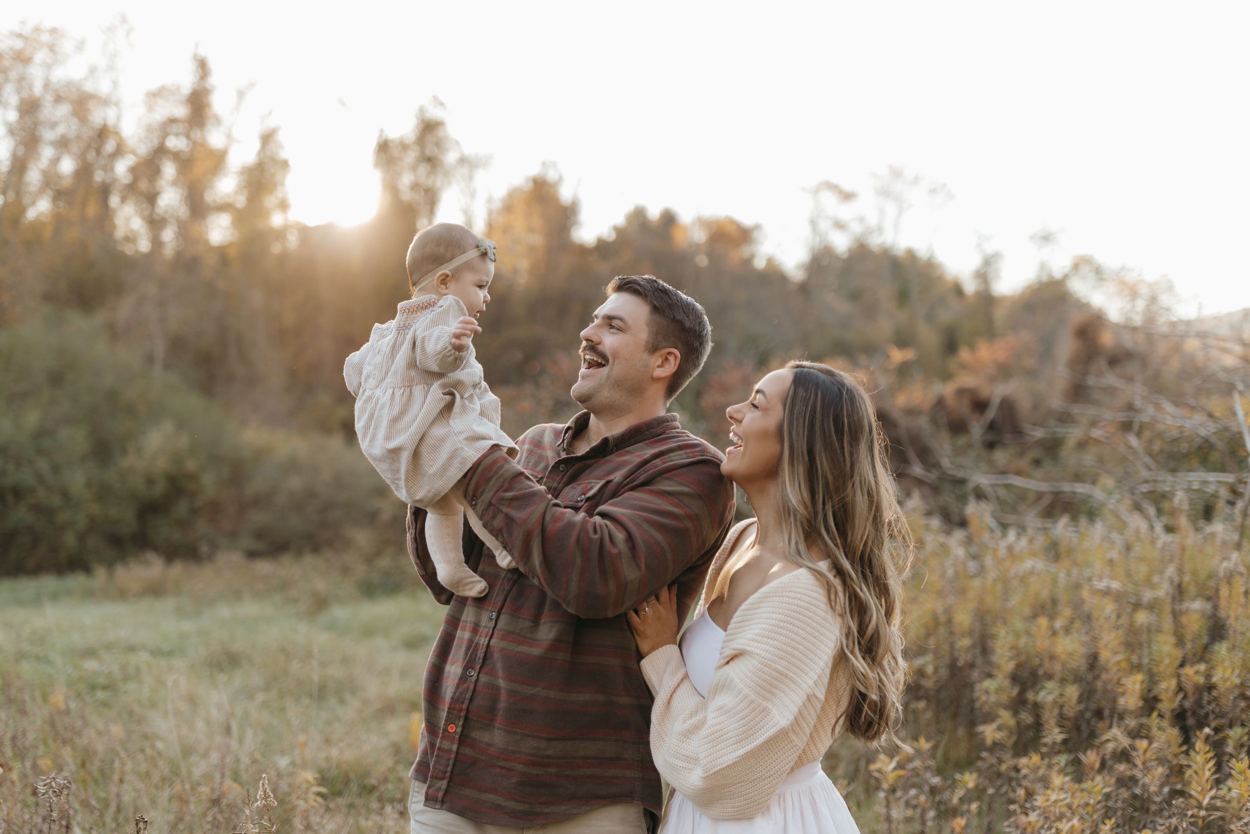 Intimate family portrait in an autumn field at golden hour showing tender moments between parents and baby.