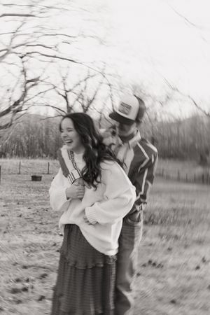 A couple in casual attire share a romantic moment dancing together in a rustic outdoor field setting.