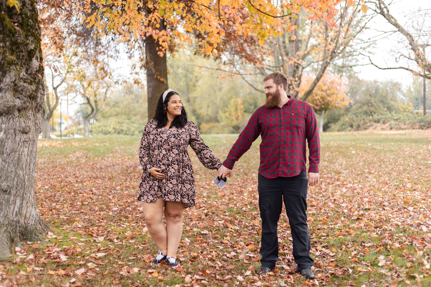 Couple enjoying a romantic autumn walk through a park filled with fallen orange and red leaves on the ground.