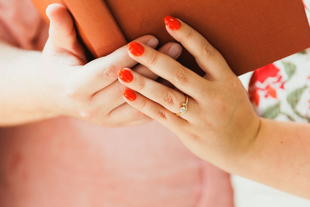 Hand with red nail polish and engagement ring resting on orange fabric.