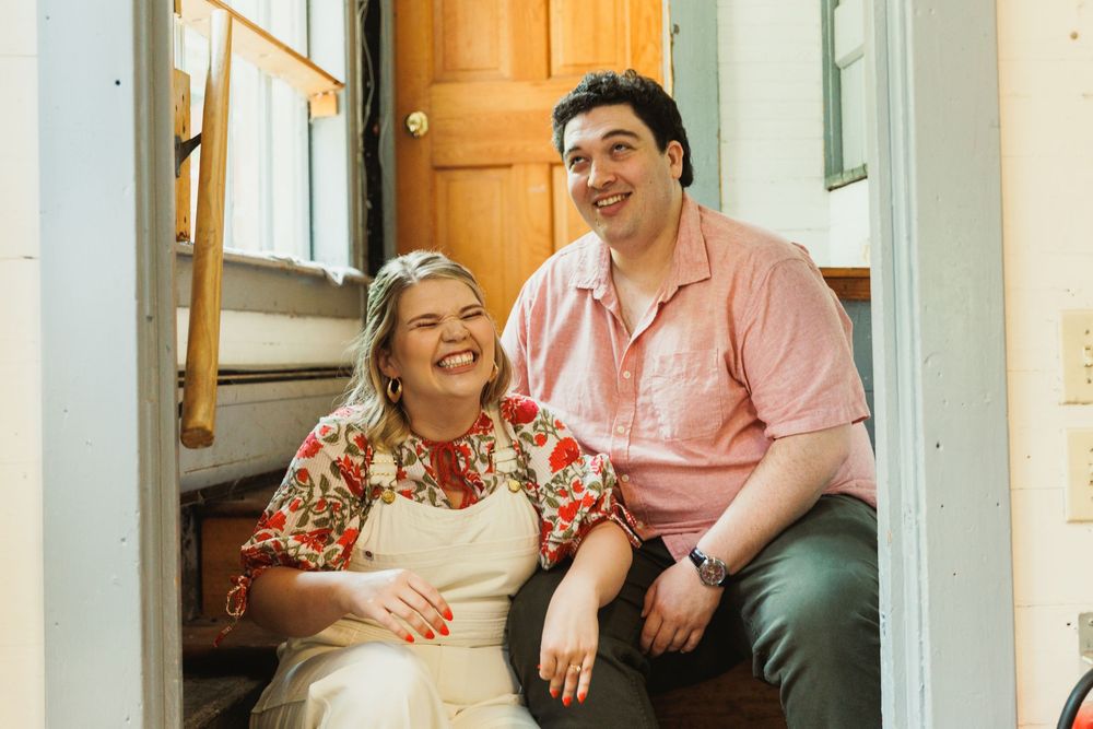 Two people sitting together on wooden stairs in a bright hallway.