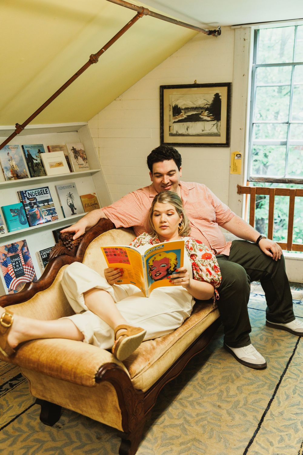 Two people reading together on a vintage brown couch in an attic library space.