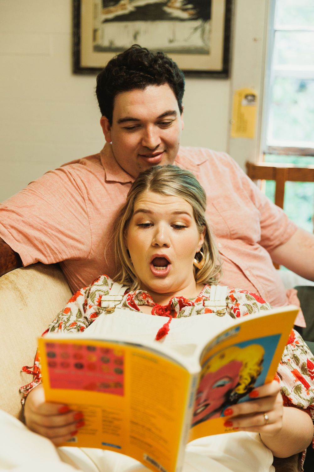 Two people sharing an animated moment while reading a colorful book on a couch.