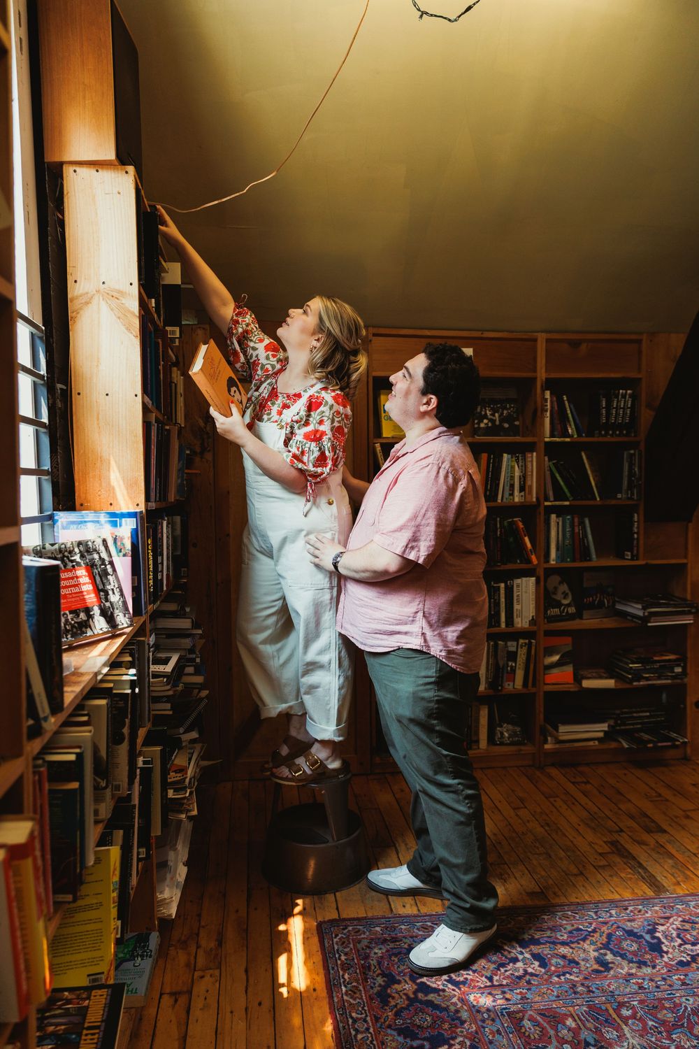 A warmly lit library scene with people reaching for books on upper shelves.