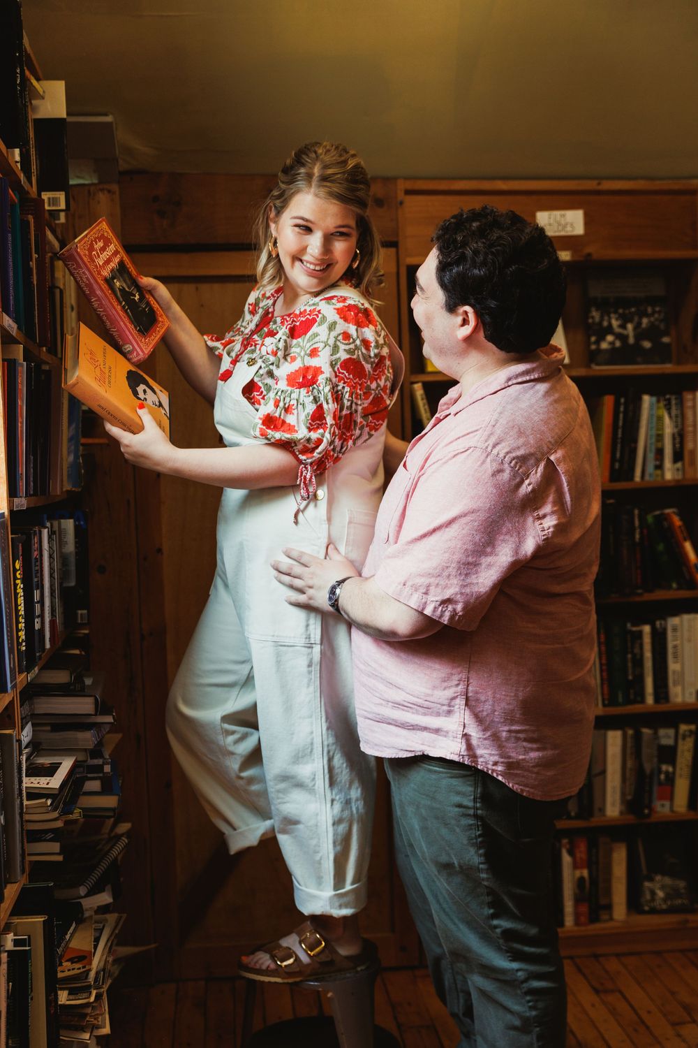 A couple browses books together in a cozy library with wooden bookshelves.