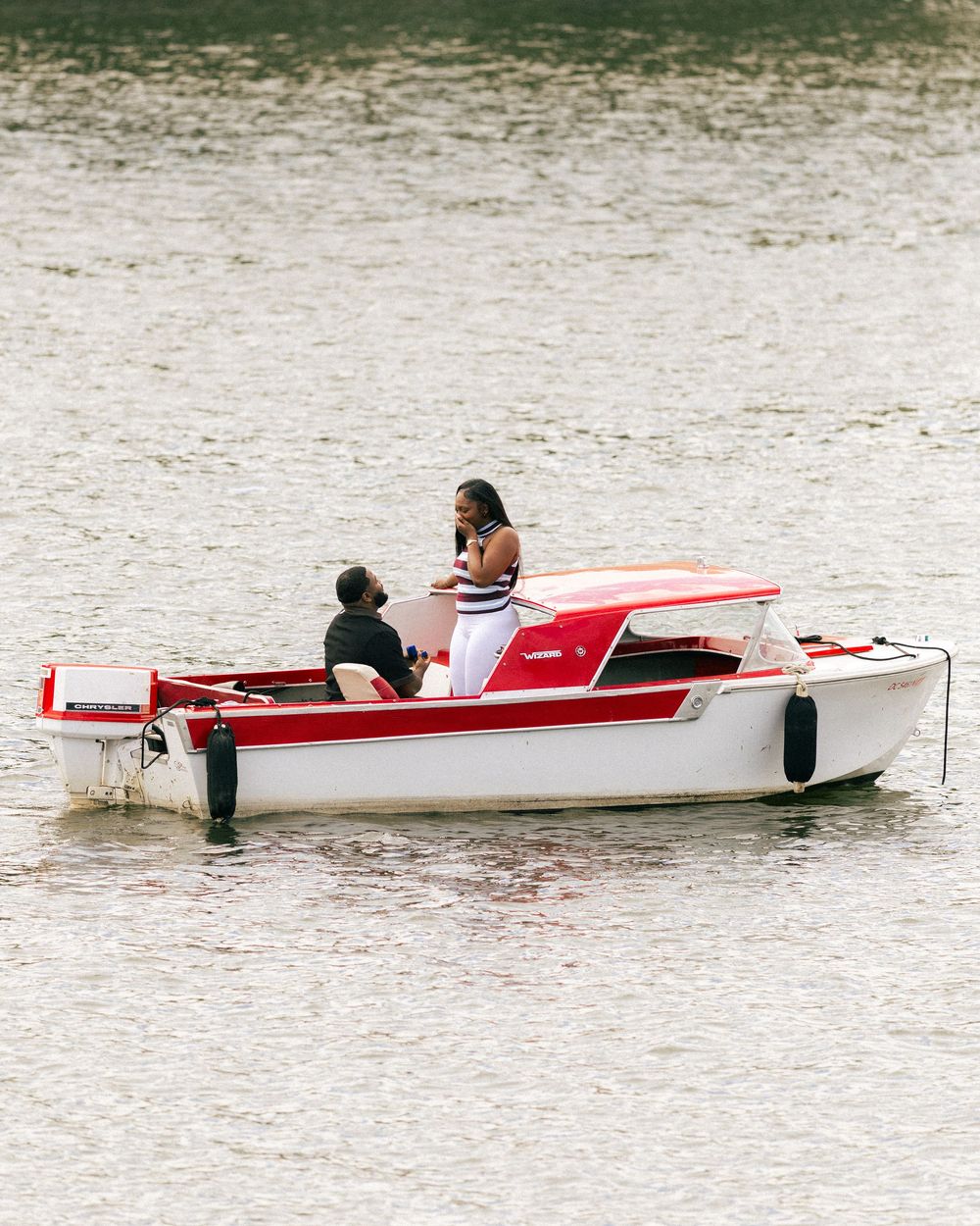 Couple enjoying a romantic boat ride on a red and white motorboat on calm water.