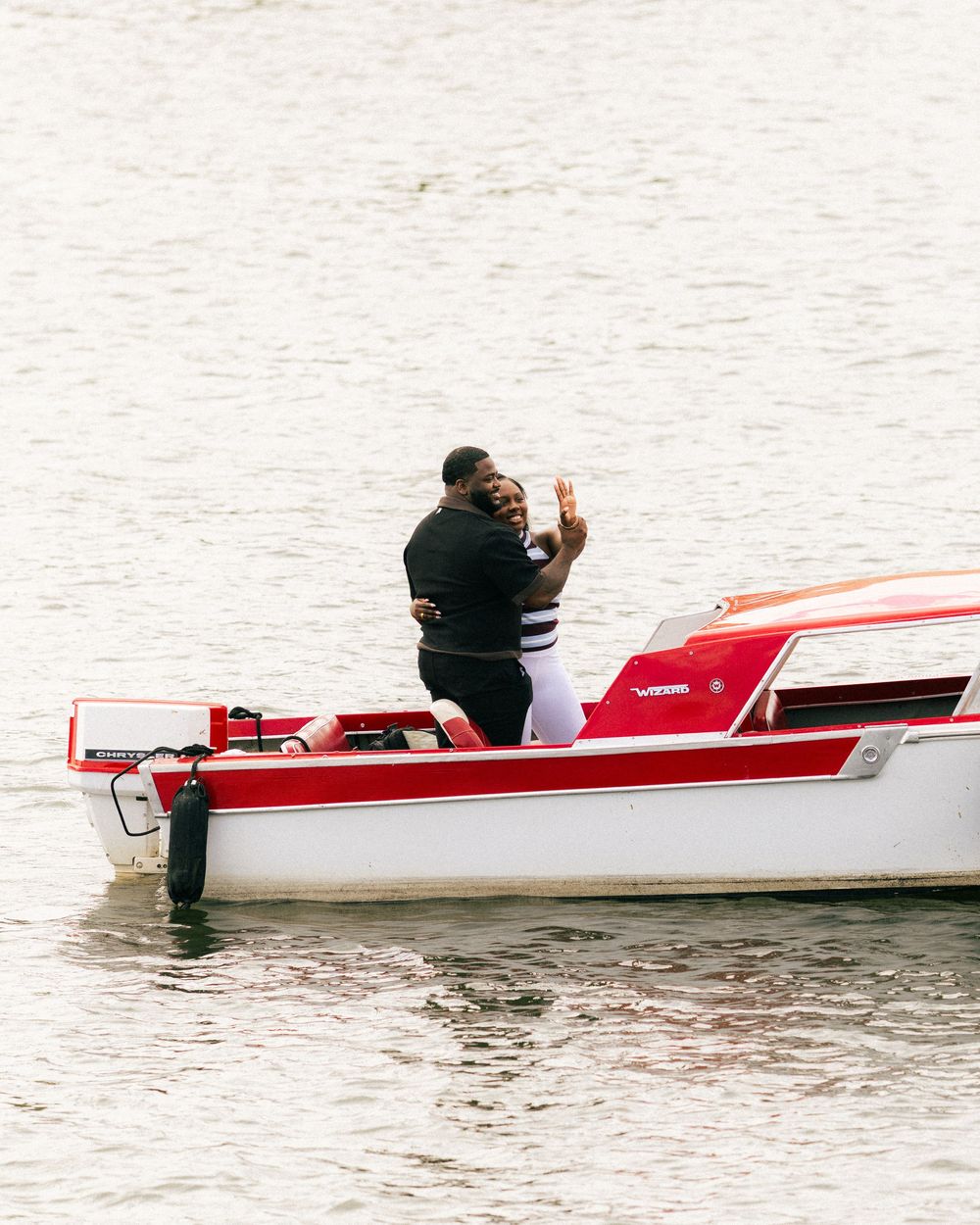 Couple embracing and taking a selfie on a red and white motorboat on calm water.