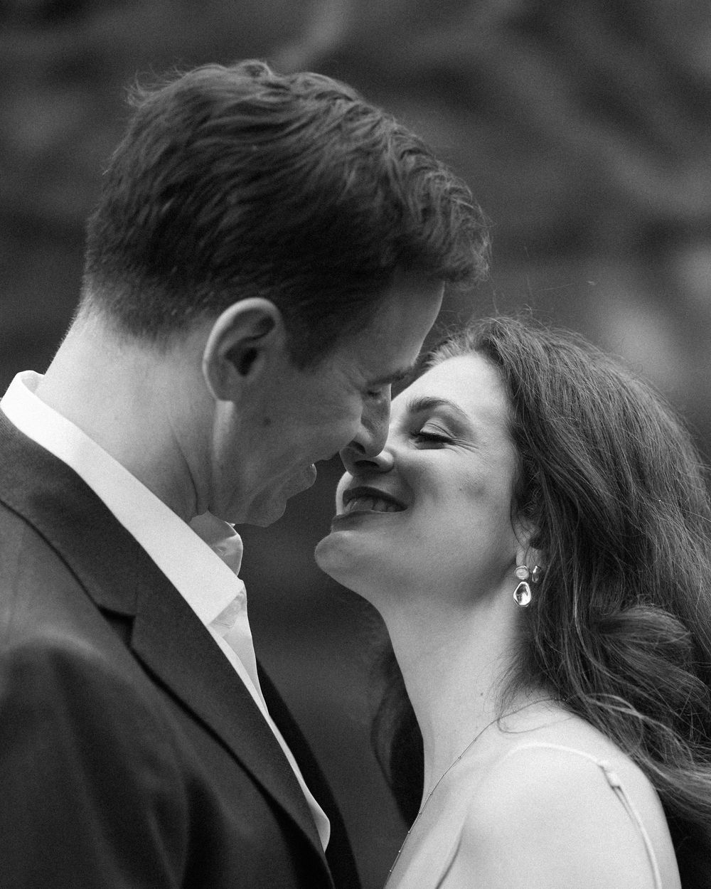 Black and white photo of a couple sharing a romantic moment, smiling and leaning in close together.