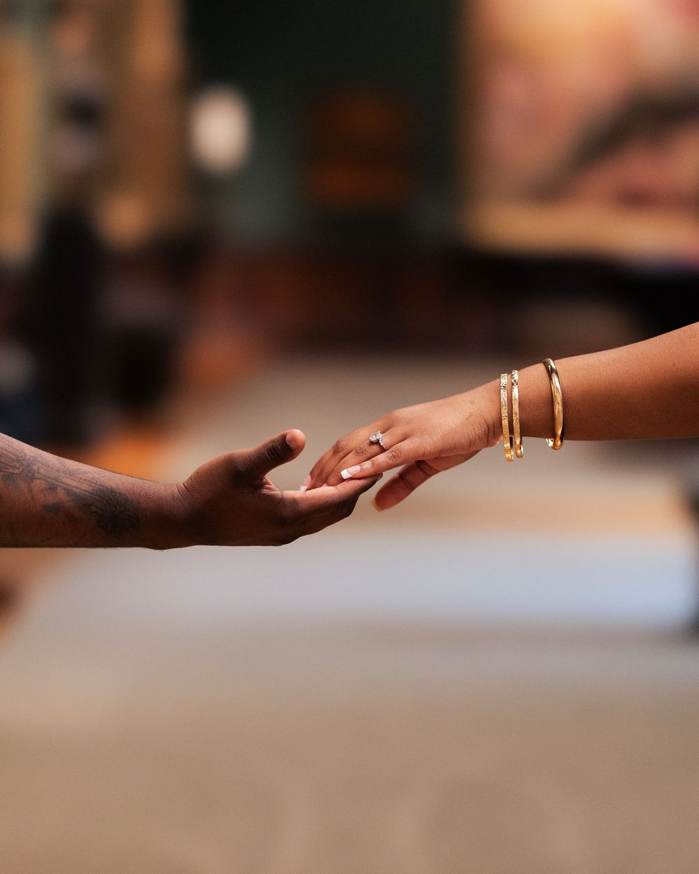 Two hands reaching toward each other, one with gold bracelets and a ring, in a tender moment of connection.