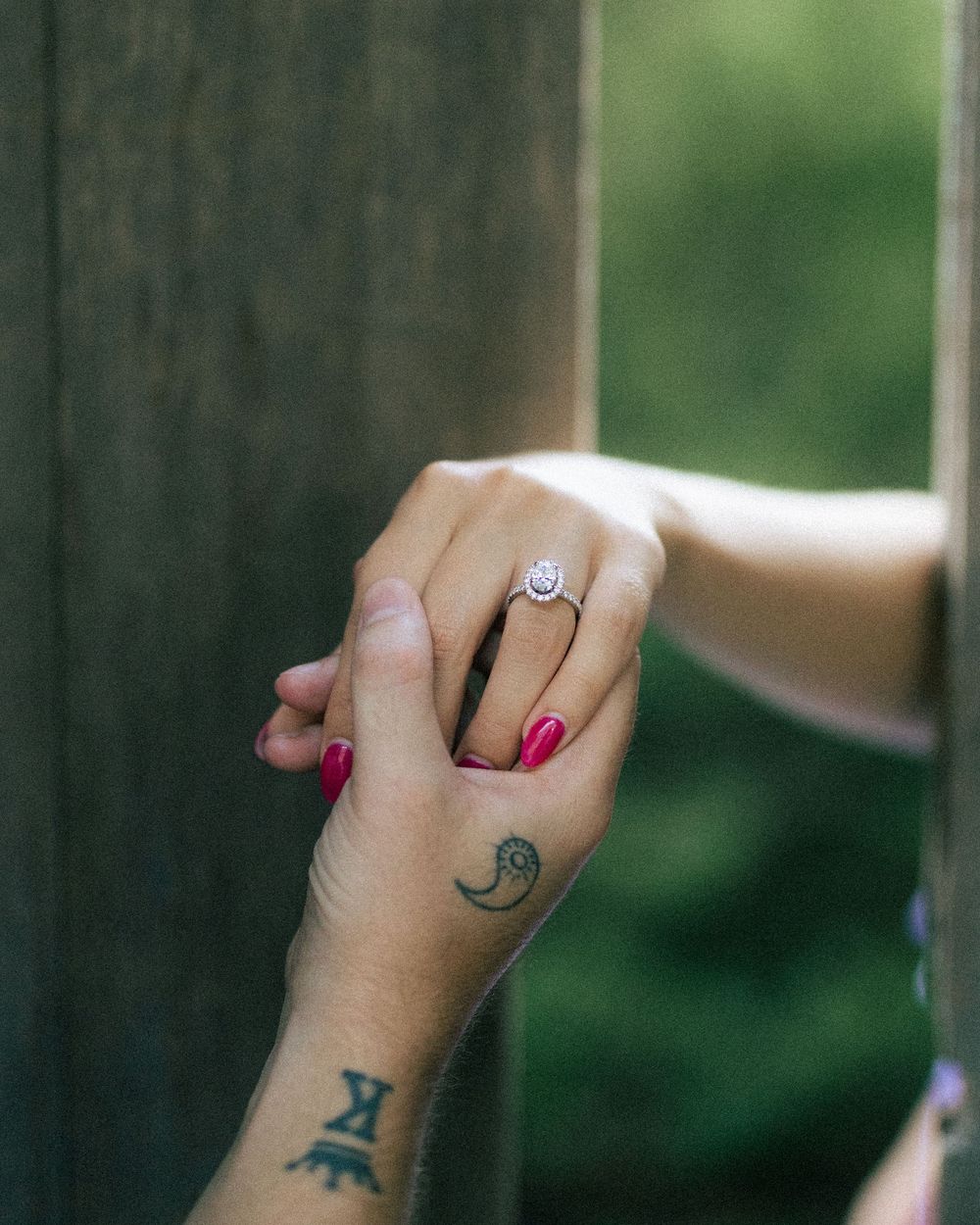Close-up of hands holding, featuring a diamond engagement ring and tattoos on the wrist.