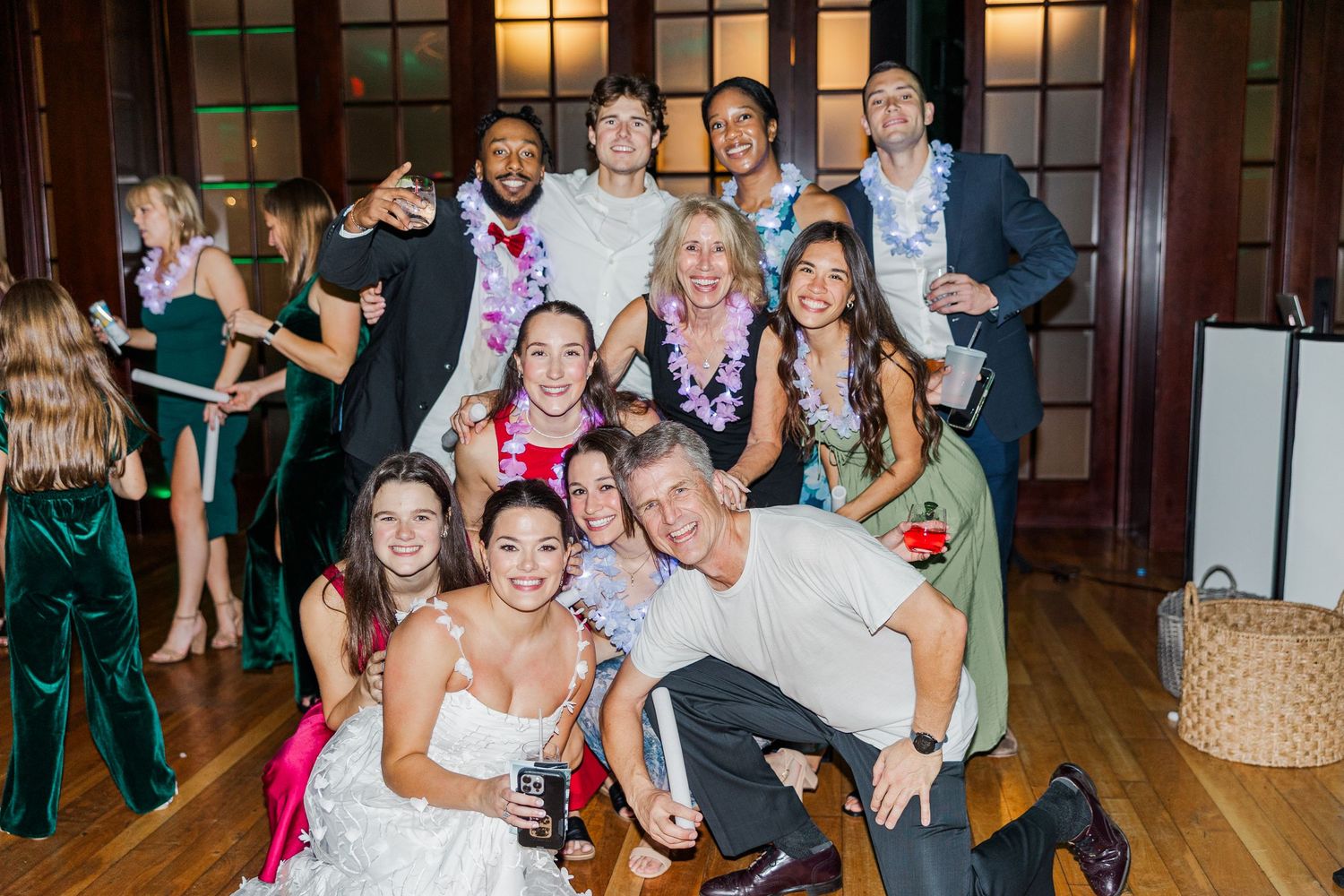 Wedding guests dance and celebrate together on a wooden dance floor in an elegant venue with warm lighting.