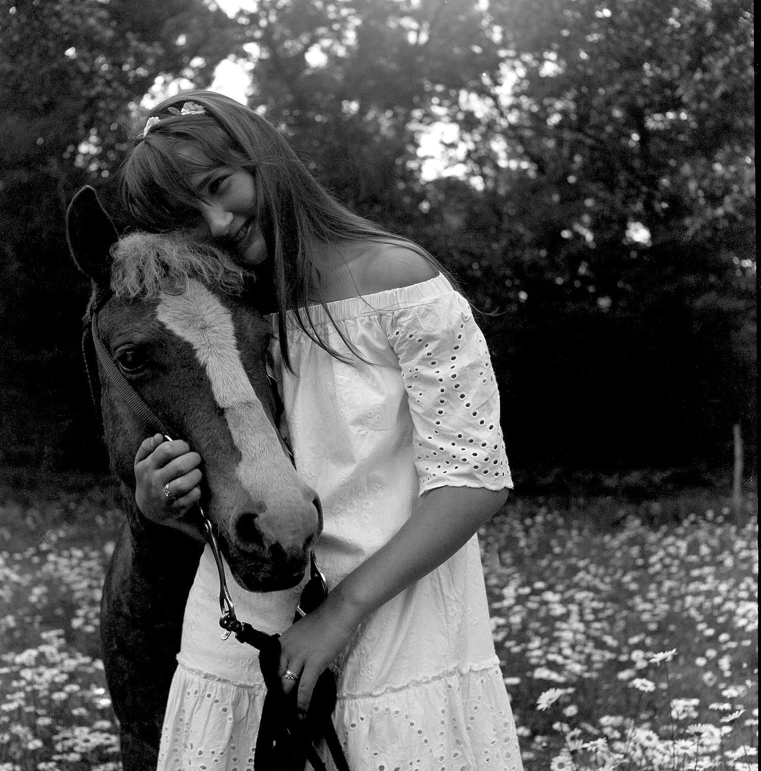 A dreamy black and white portrait shows an intimate moment between a person and horse in a flower field.
