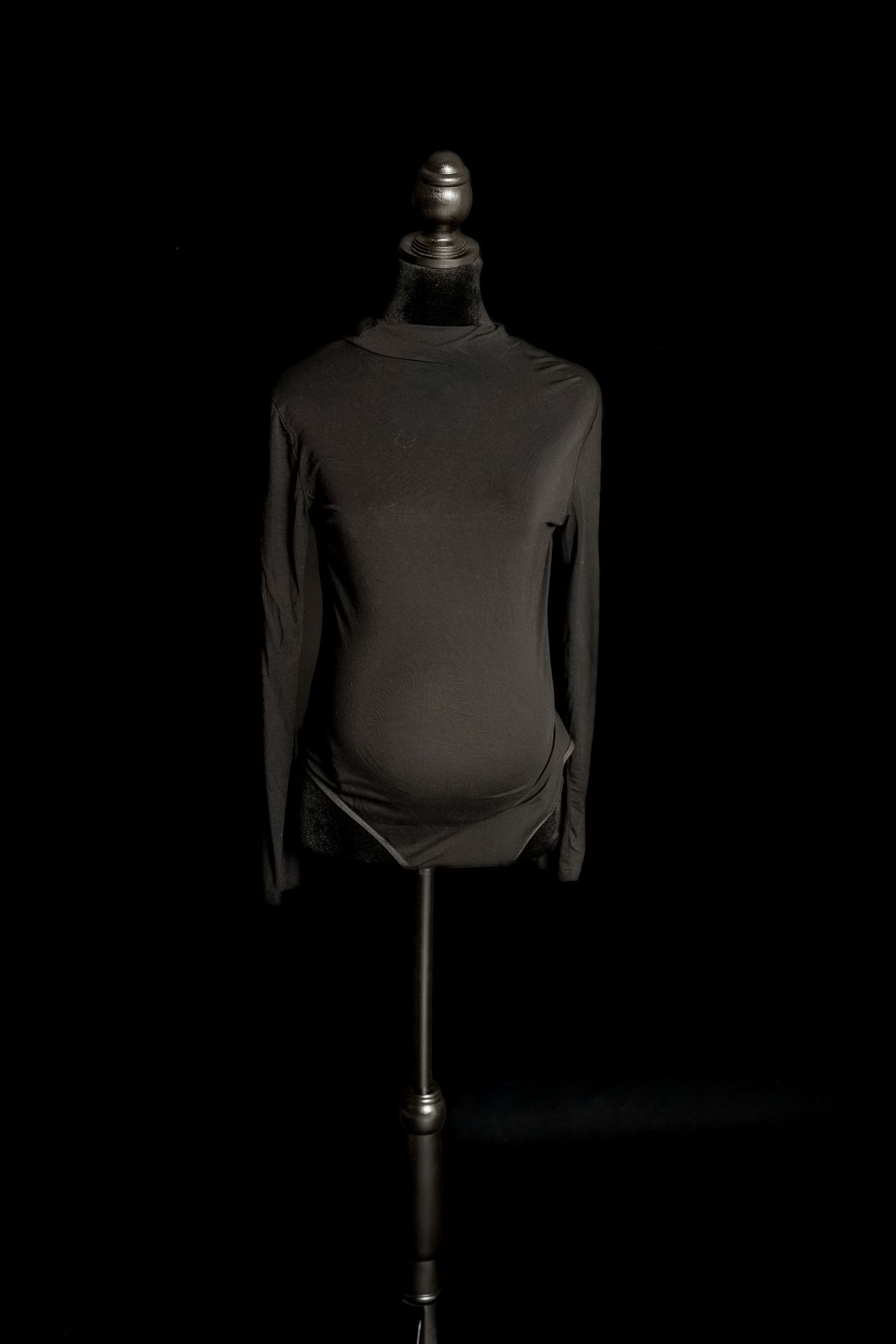 Black long-sleeve maternity bodysuit with high neckline and fitted silhouette on a dress form.