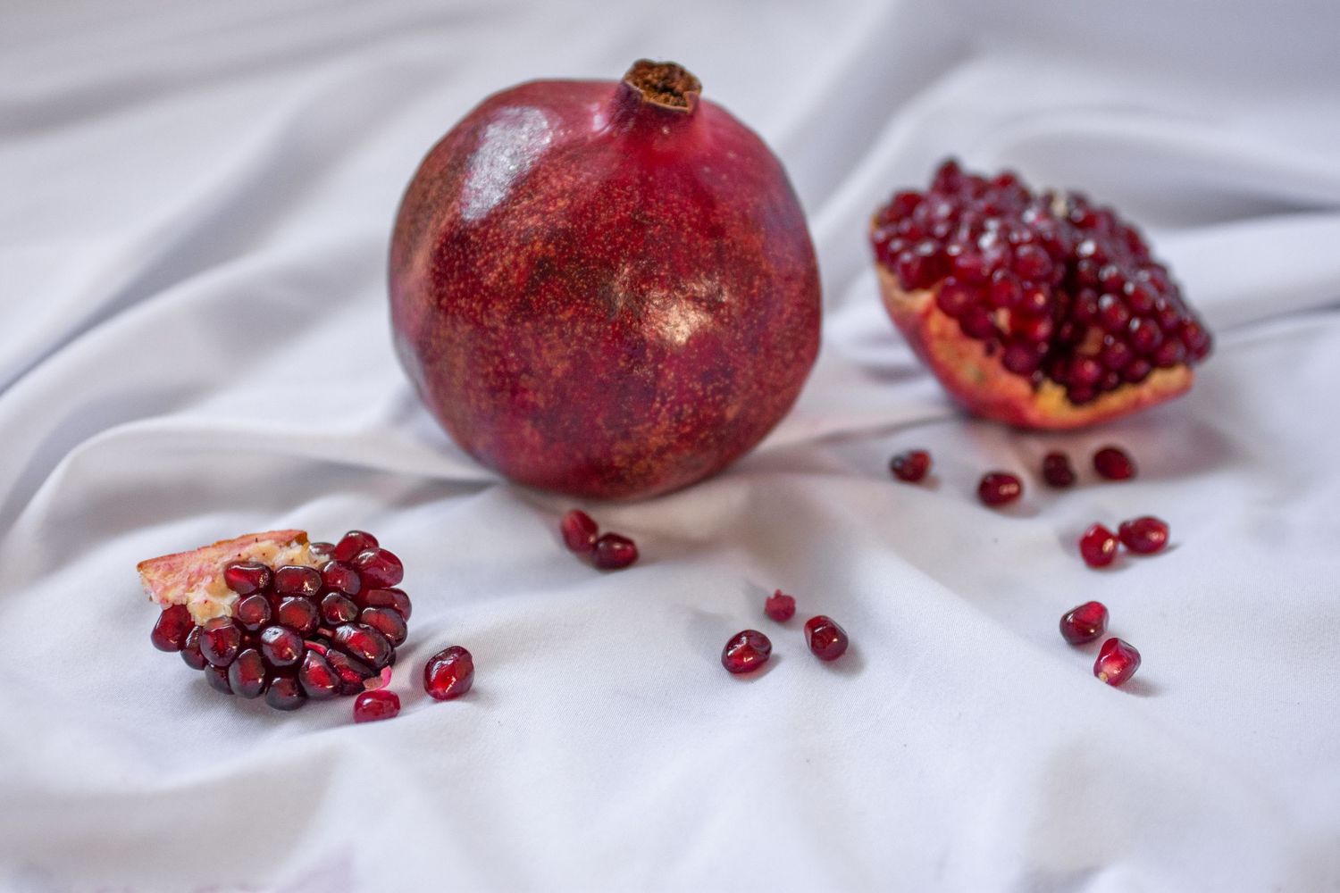 Fresh pomegranates and scattered seeds arranged on white fabric in an artistic still life for branding photos.
