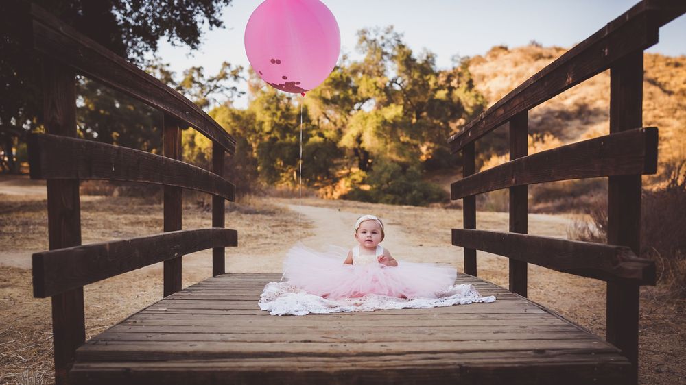 Pink balloon floating above wooden boardwalk at sunset with warm golden light filtering through trees.