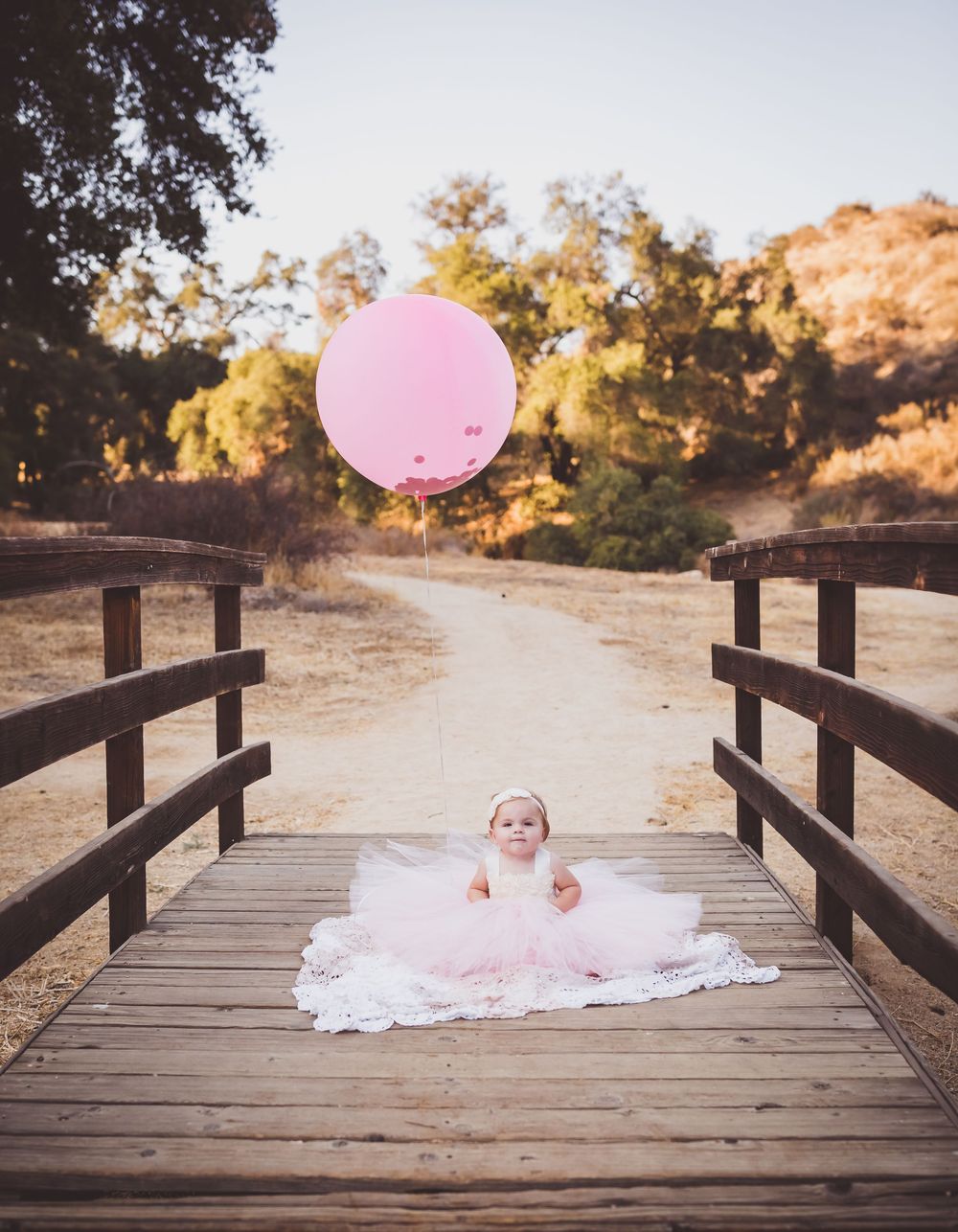 A pink balloon floats above a wooden bridge walkway in a scenic outdoor setting during golden hour.