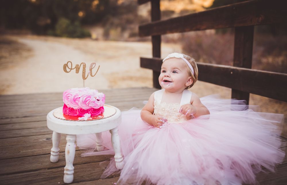 A pink tulle dress and white candle holder with 'one' text displayed on a wooden deck surface.