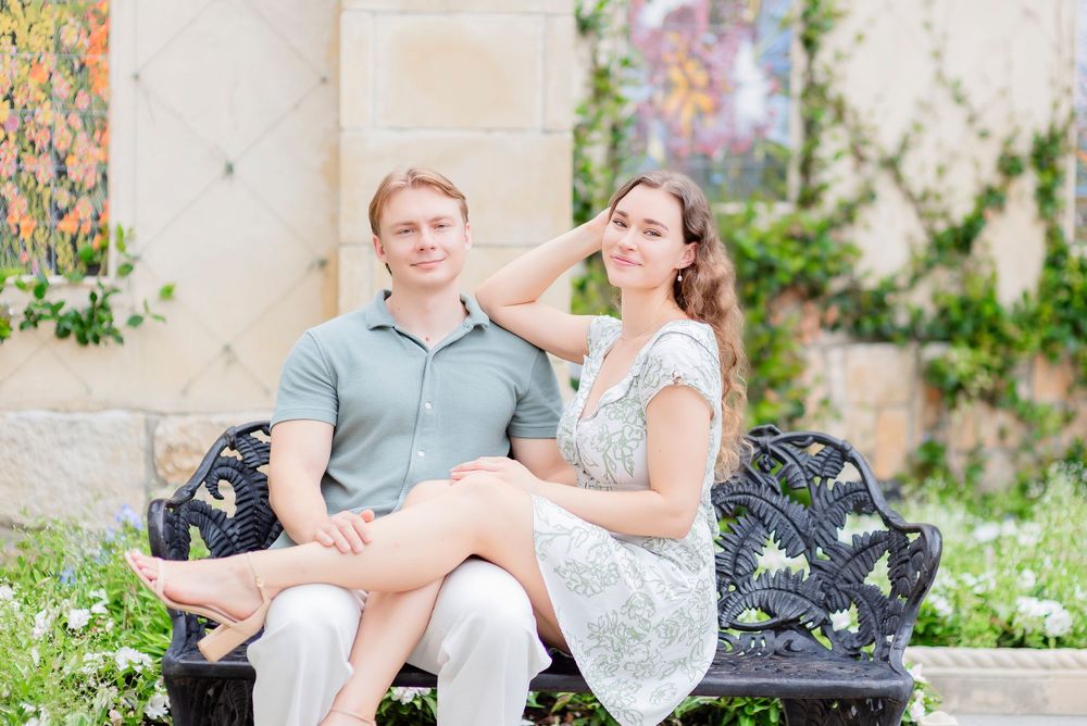 A couple sits together in a garden setting wearing formal attire during a romantic photoshoot.
