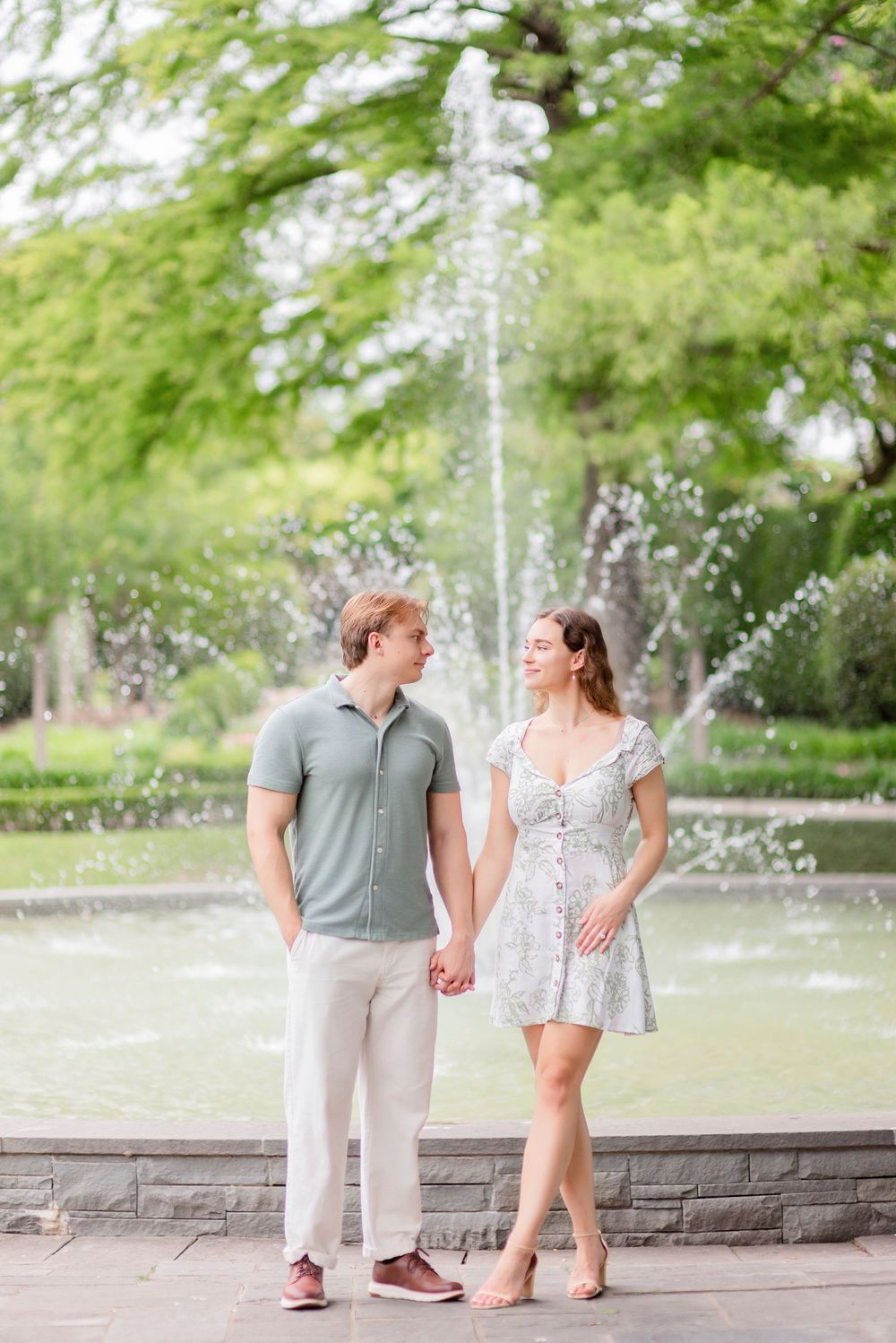 A romantic photoshoot by a fountain with lush green trees creating a natural backdrop.