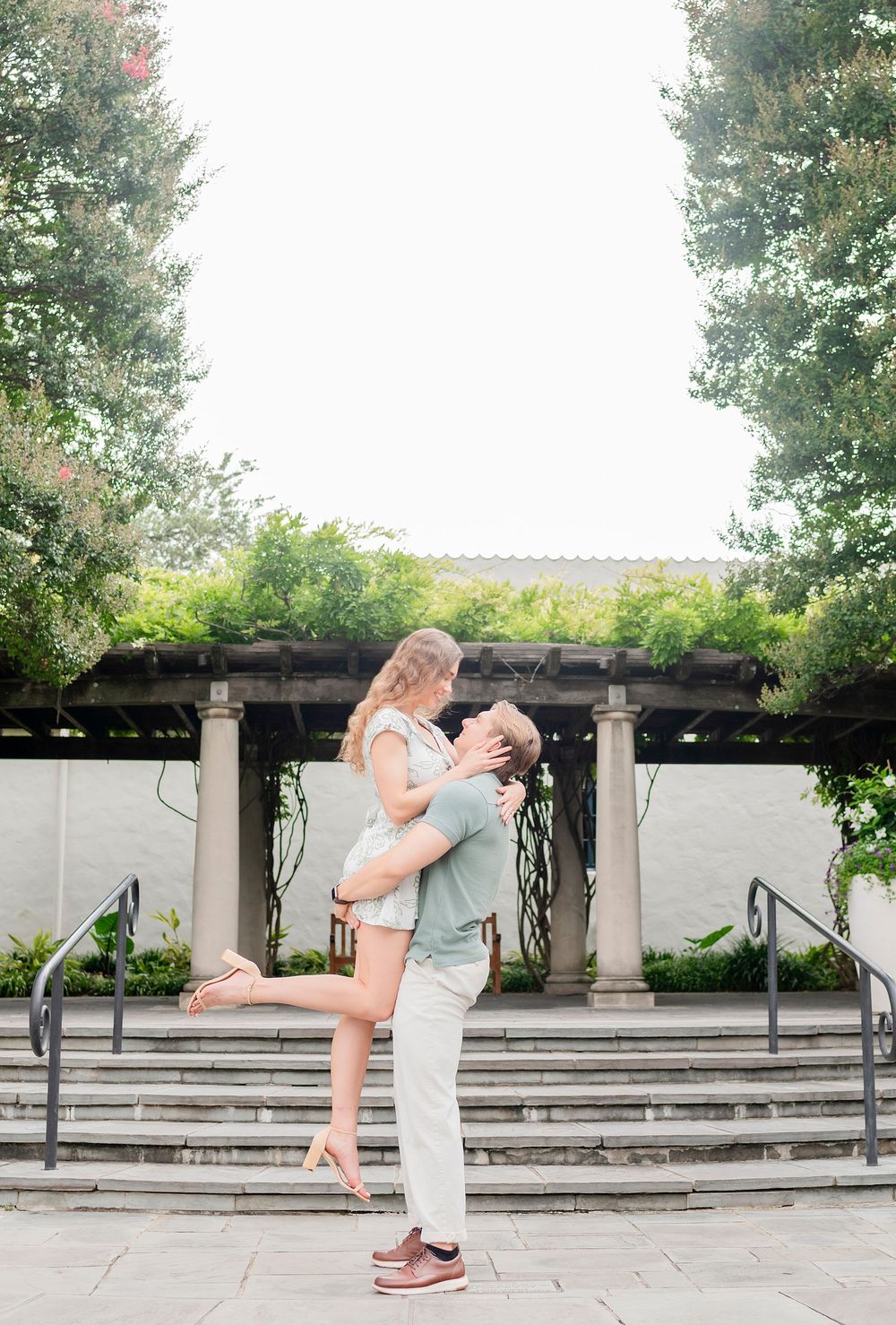 A couple shares a playful moment in front of stone columns and steps in an outdoor garden.