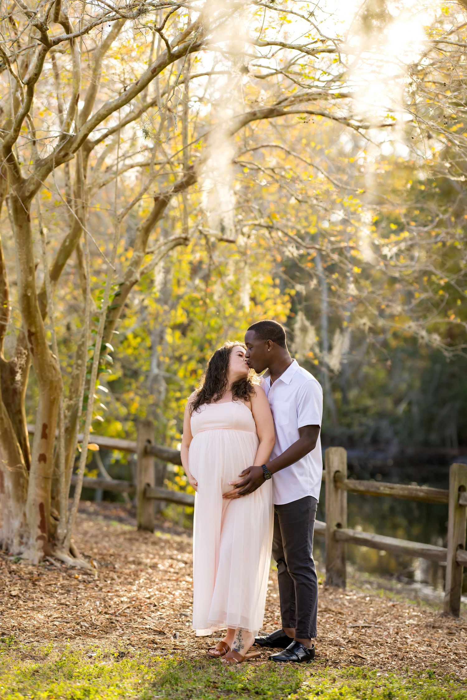 A couple shares a romantic moment in a sunlit autumn forest with golden leaves and natural scenery.