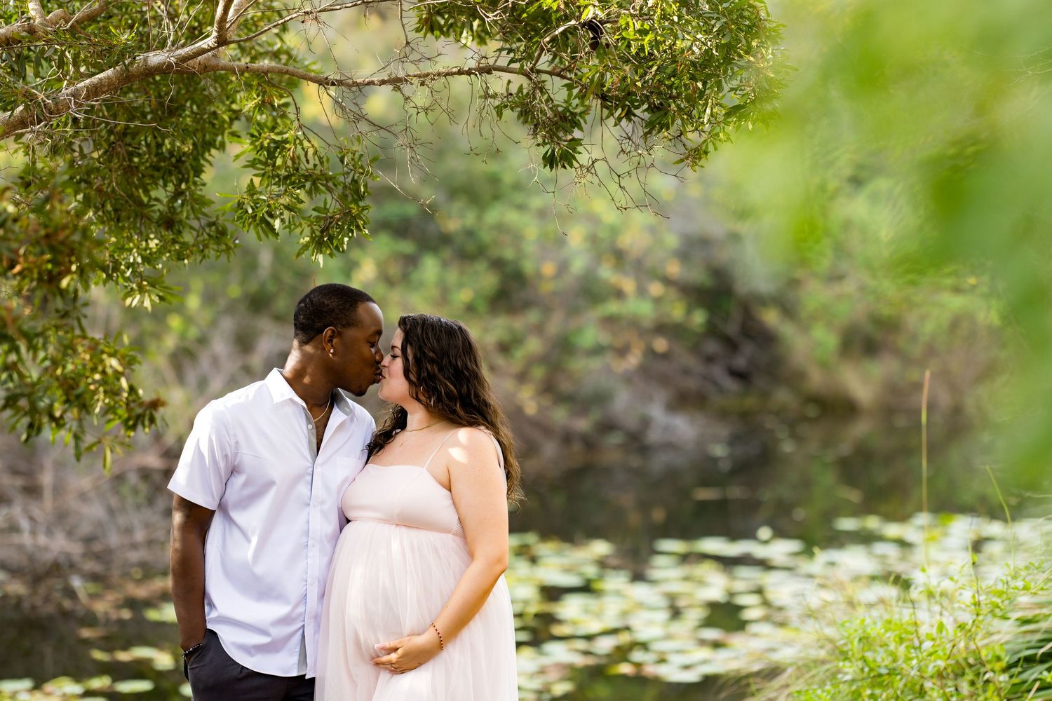 Couple embracing in a romantic garden setting surrounded by lush greenery and a serene pond.
