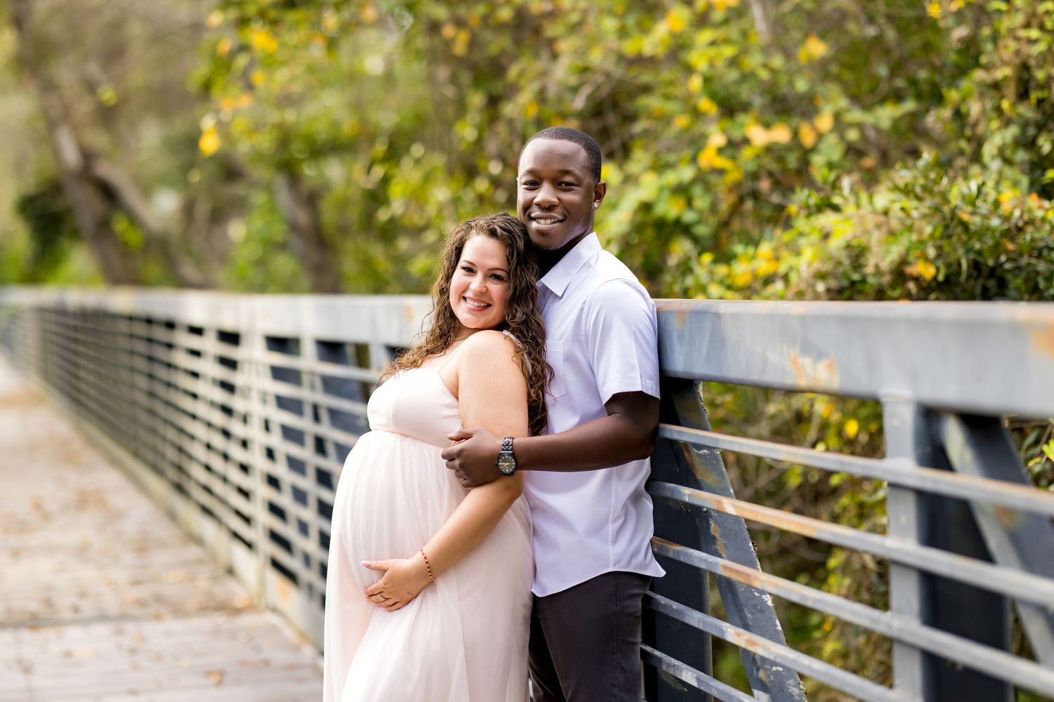 A couple shares a romantic moment while sitting on a wooden bench surrounded by lush greenery and autumn foliage.