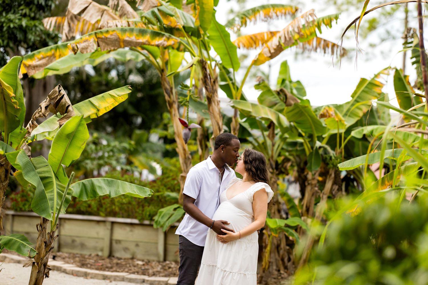A couple shares an intimate moment in a lush tropical garden with banana trees and greenery surrounding them.