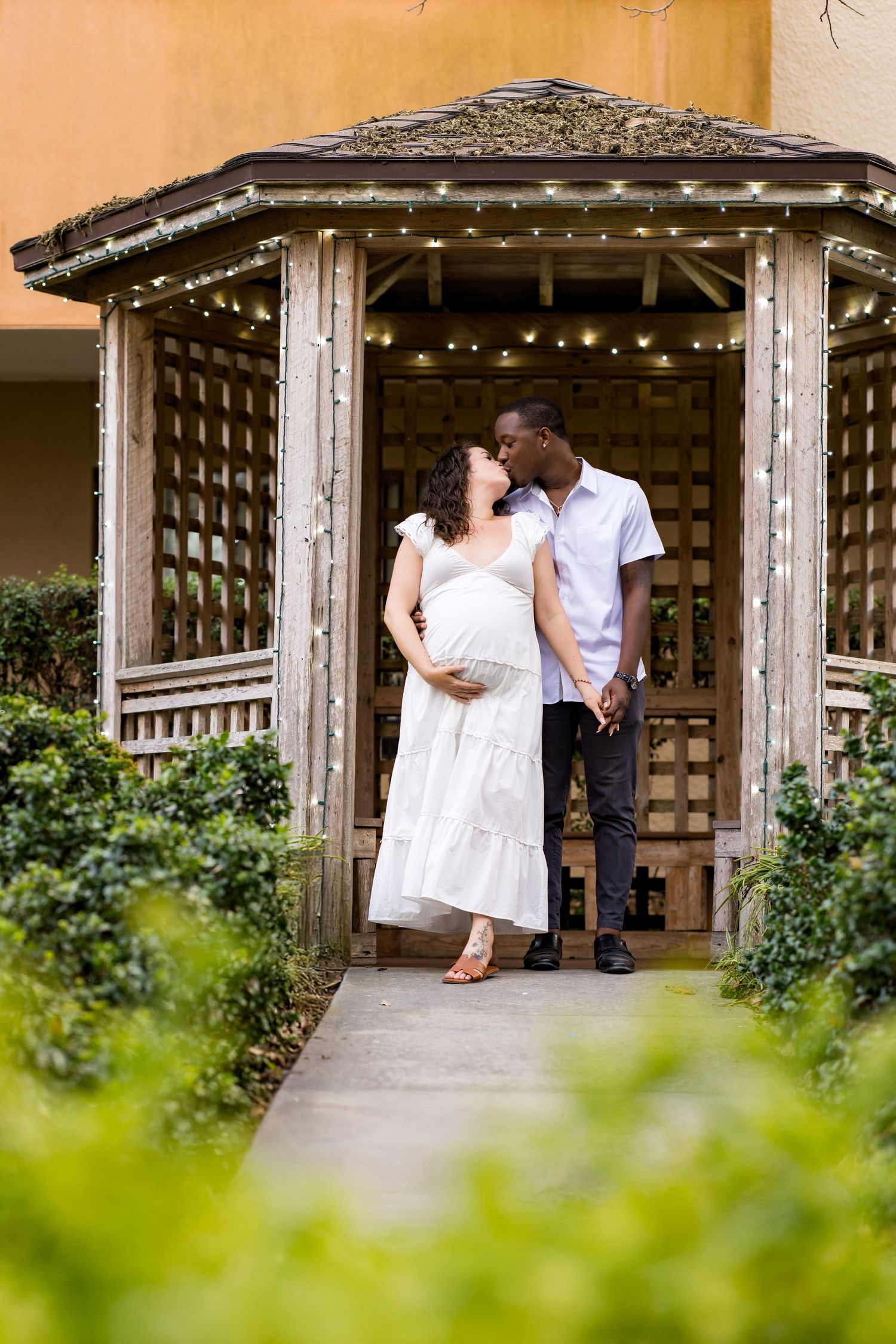 A romantic couple shares an intimate moment on a rustic wooden bench in a garden gazebo.