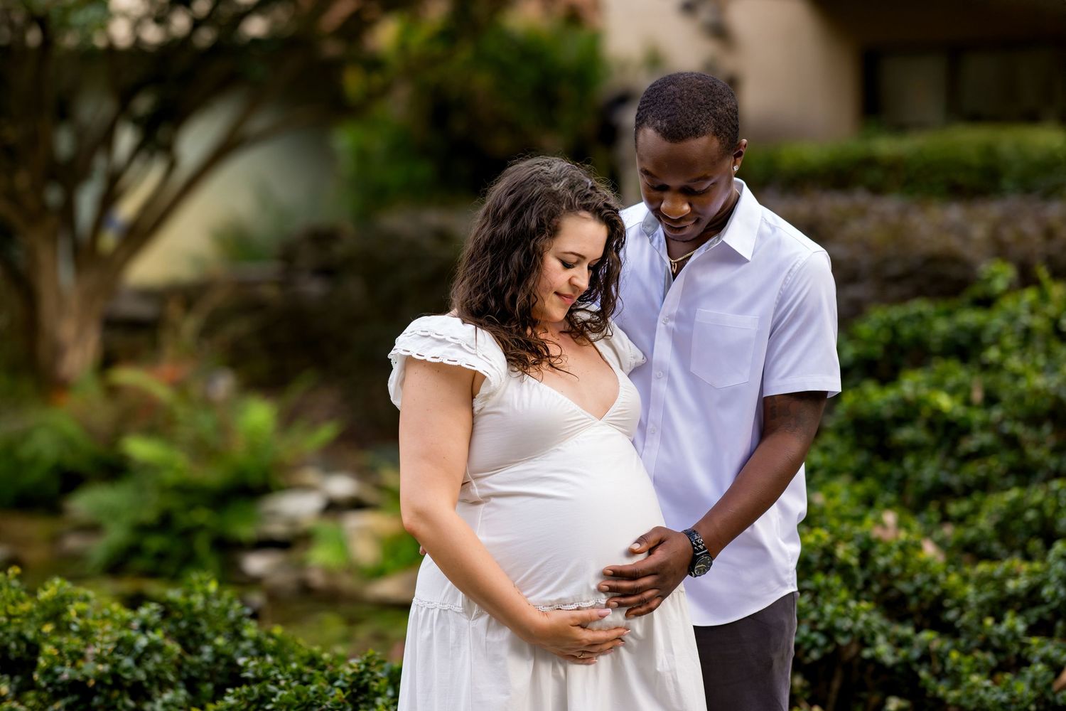 A couple in white attire shares tender moments together in a lush garden setting during a romantic photoshoot.