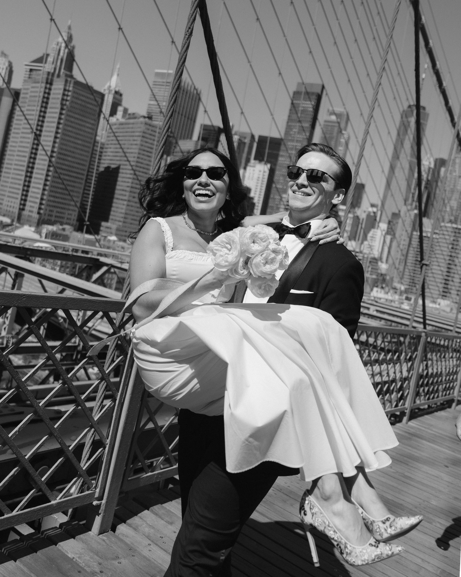 Wedding couple sharing playful moments on Brooklyn Bridge with Manhattan skyline in background.
