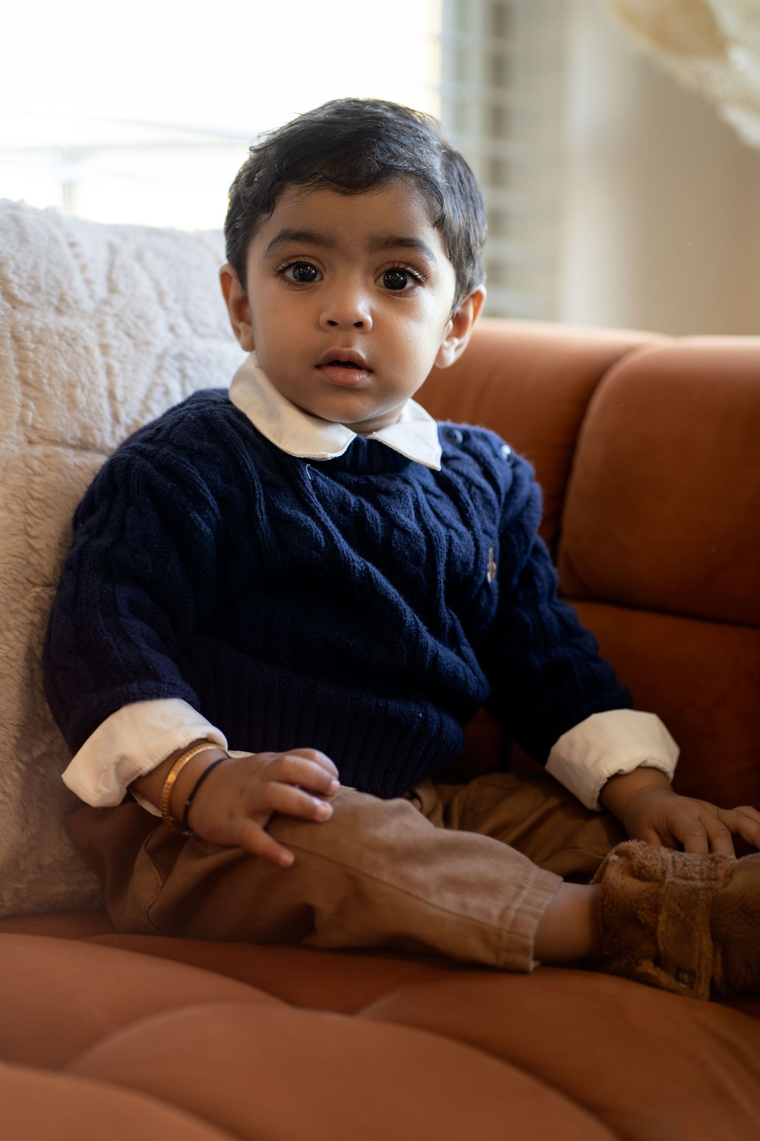 A young child in a navy sweater lounges on a brown leather couch in a series of candid poses.