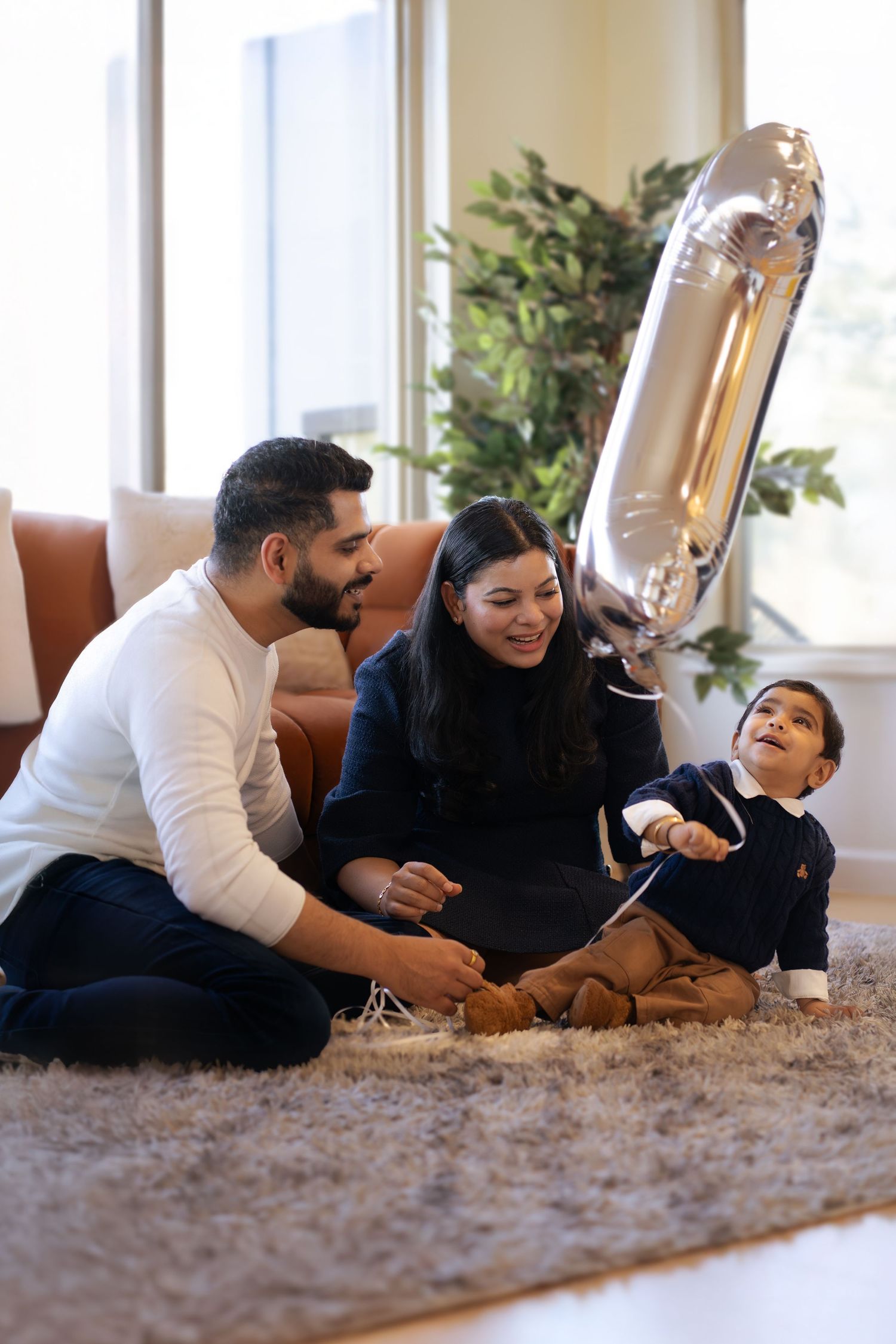 Family celebrating with a silver number balloon while sitting together on plush carpet in living room.